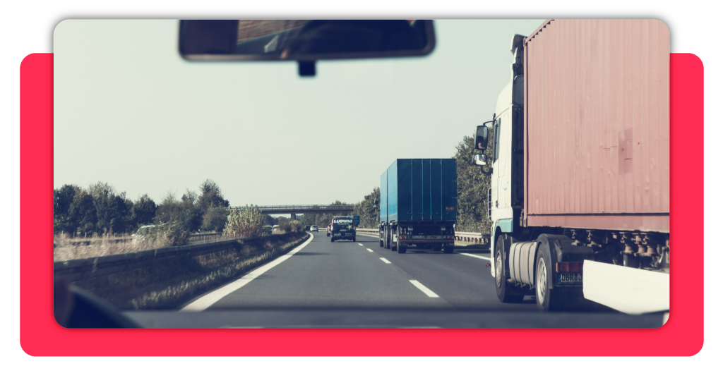Dos camiones de transporte de mercancía transitan con normalidad por una carretera durante el día. A la izquierda se observa un vehículo familiar.