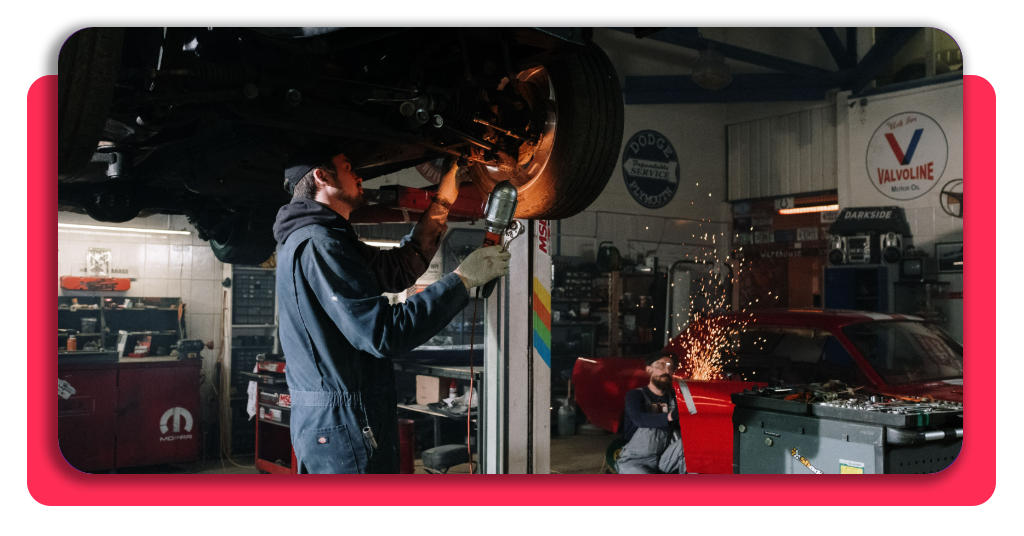 un par de hombres están trabajando en un taller mecánico. Uno se encuentra realizando labores de soldadura, mientras que el otro observa un neumático.