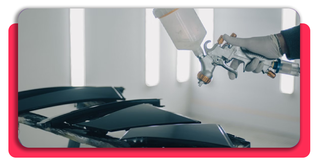 Curso 100% GRATIS de pintura de coches con clase práctica 2 Un hombre pintando unas piezas automotrices, primer plano de su mano y la herramienta que utiliza para pintar